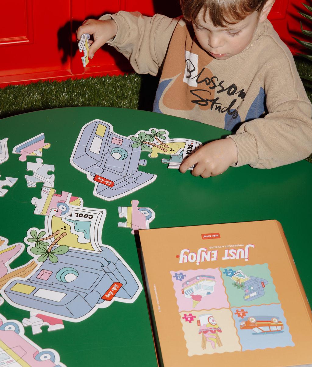 Garçon assemblant un des quatres puzzles format appareil photo, sur une table - photo lifestyle - Hello Hossy